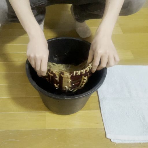 グローブをバケツのお湯に浸ける様子